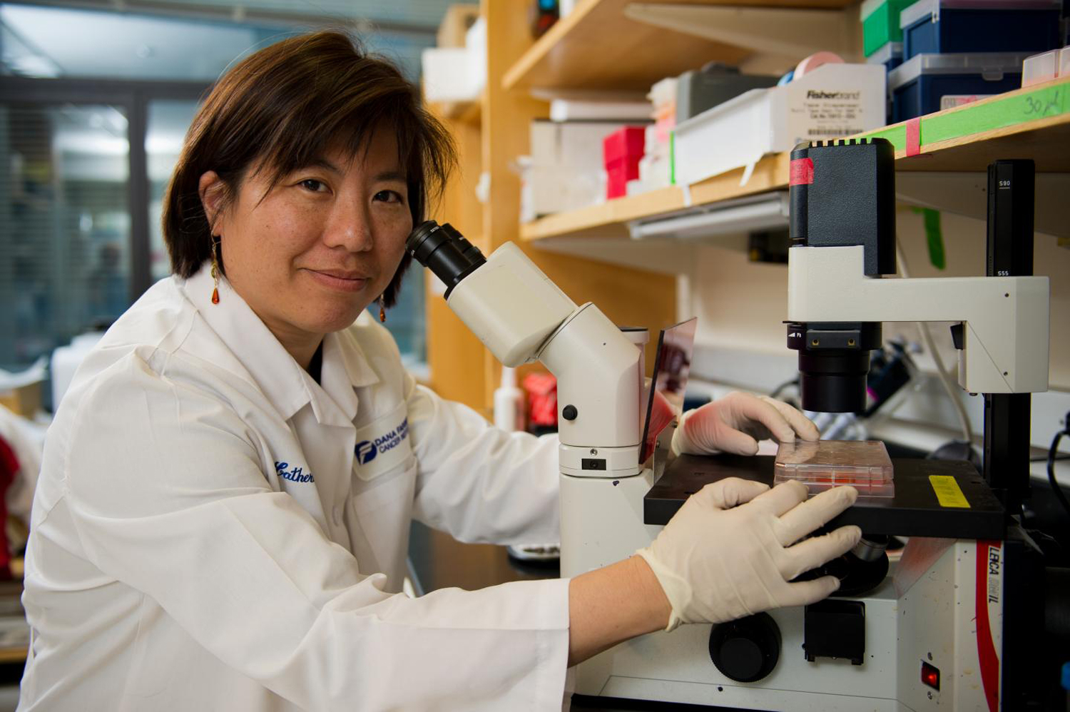Dr. Catherine Wu looks at the camera while sitting at a microscope.