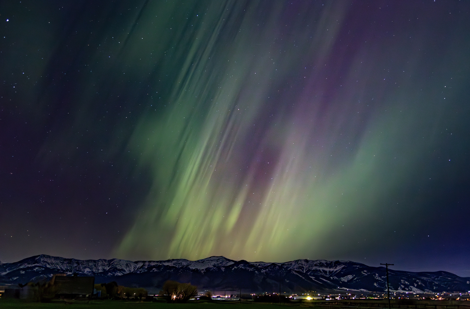 Dramatic streaks of green and purple in the night sky above mountains