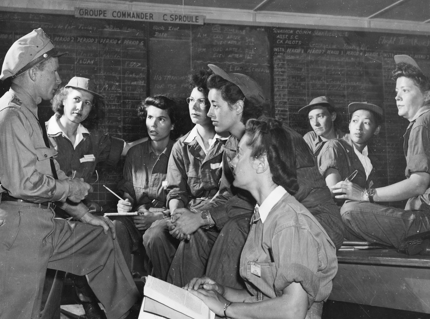 Hazel Ying Lee and a group of women wearing jumpsuits and hats listen to a man in uniform who is speaking to them.