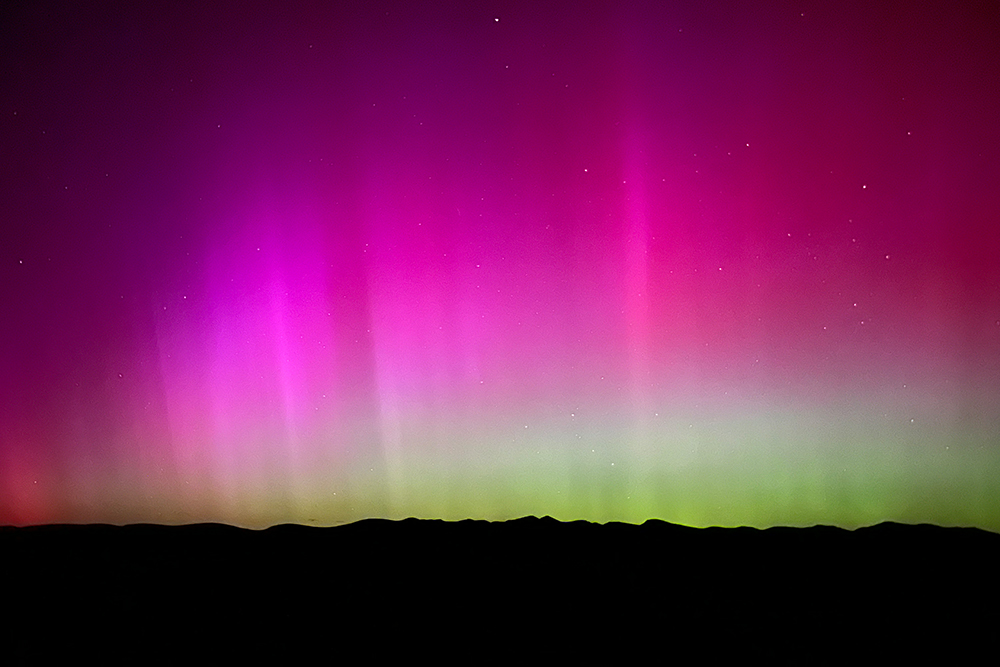 A bright pink and green night sky above silhouetted hills