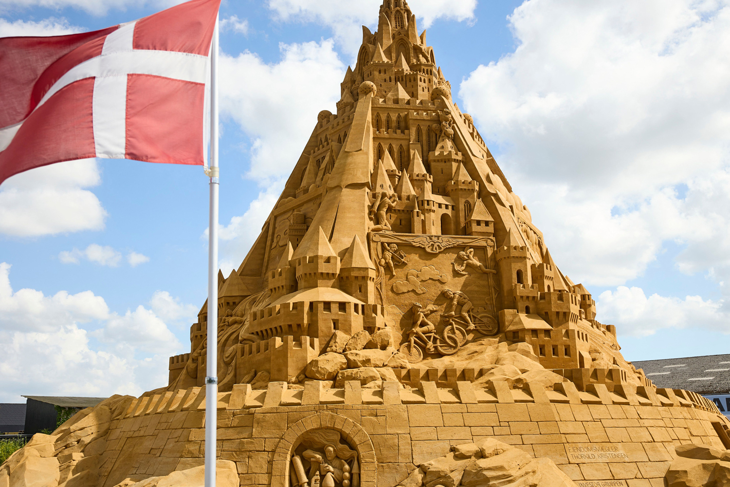 A large sandcastle with many turrets and an image of Cupids and people on bicycles.