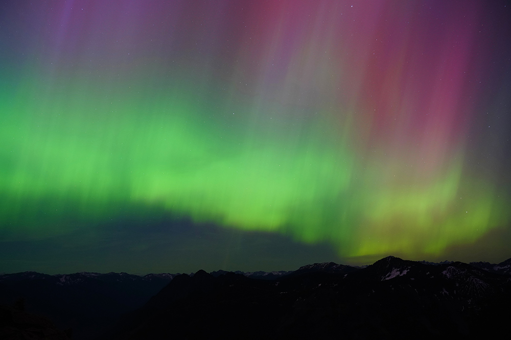 A night sky with streaks of green and pink above a hilly landscape