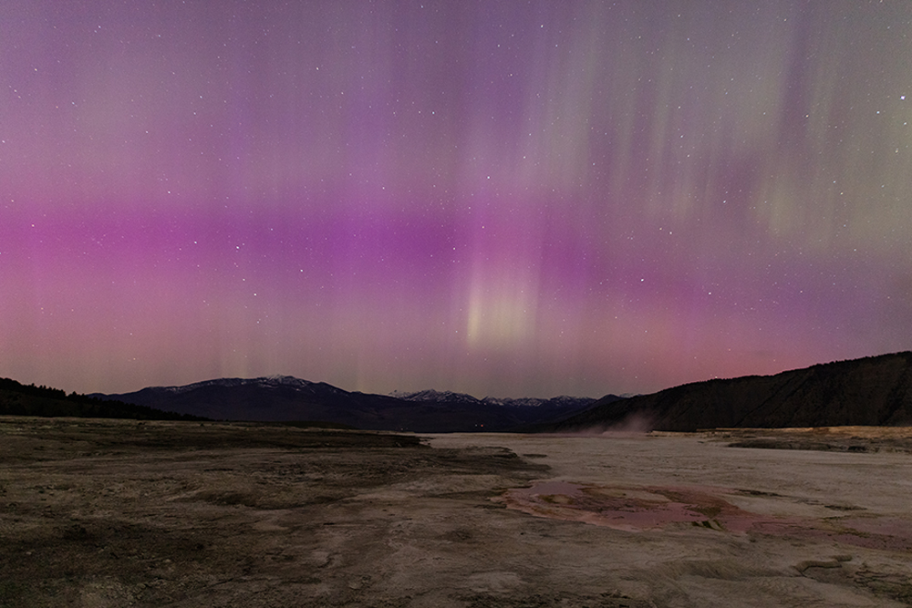 Streaks of purples and pinks in the night sky above a rugged landscape