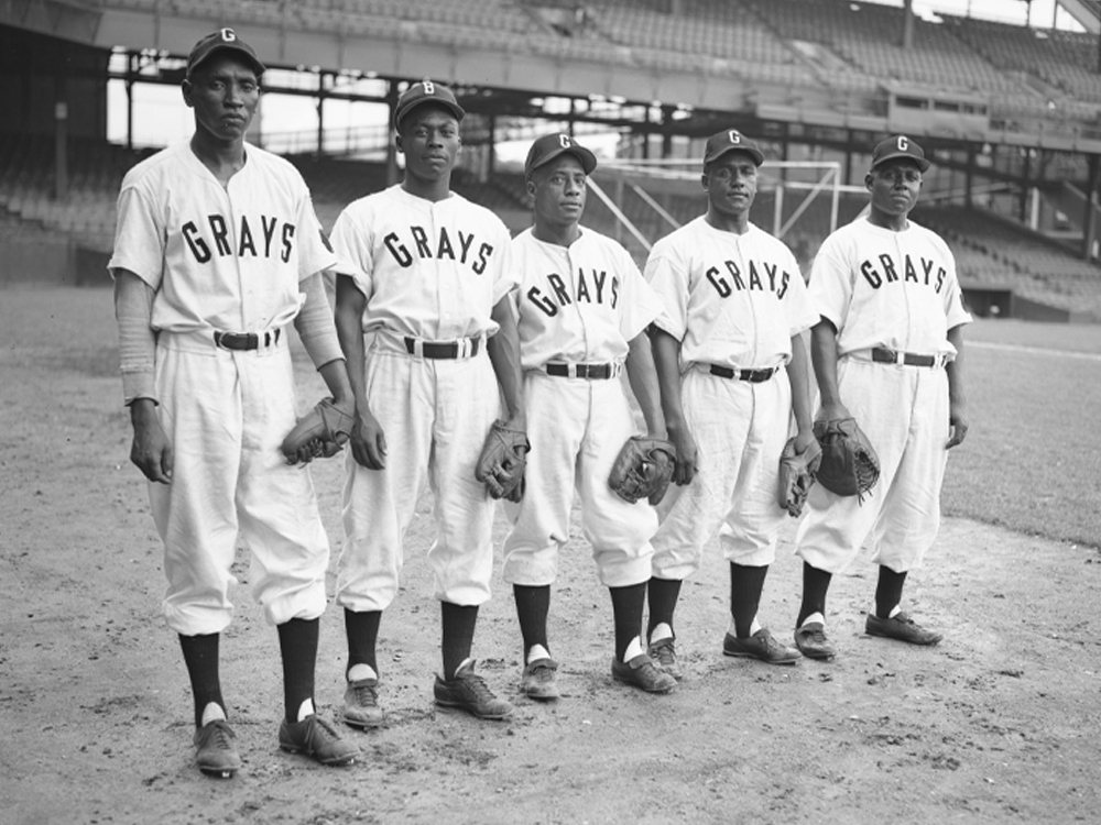 Five ball players in Grays uniforms and holding gloves pose on the field.