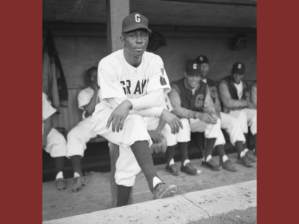 Victor Harris poses while facing out of the dugout with players in uniform behind him.