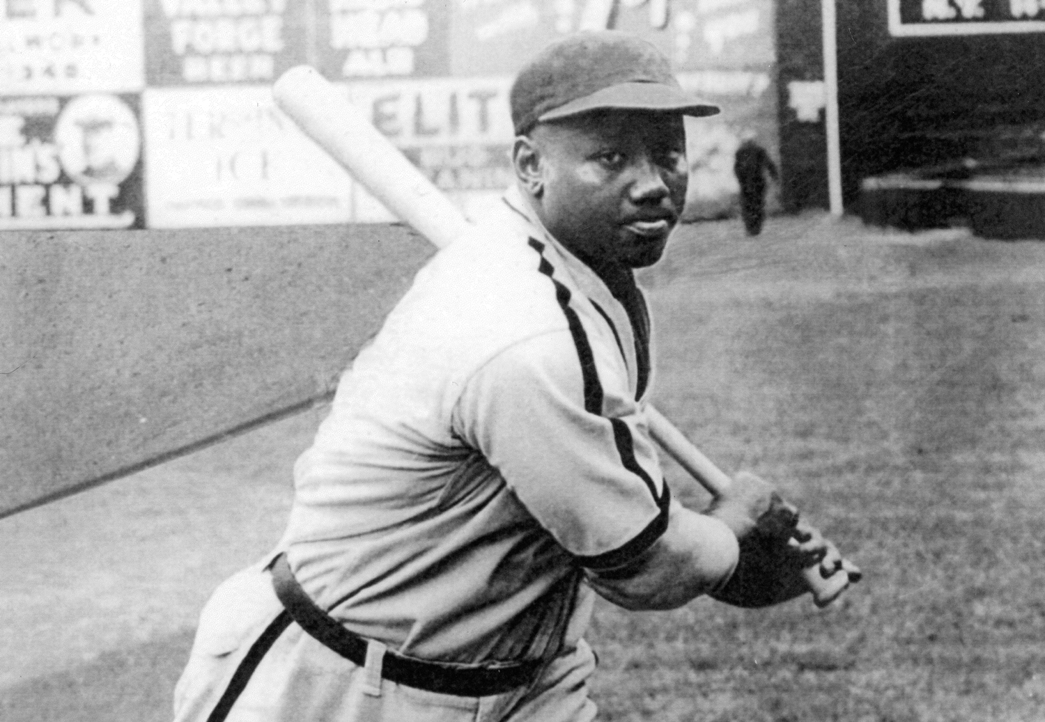 Josh Gibson stands on a baseball field, poised to swing a bat.