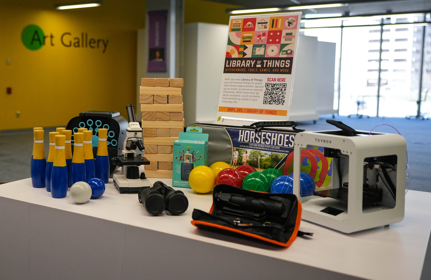 Bowling pins, a 3D printer, horseshoes, binoculars, and more are on a table under a sign that says Library of Things