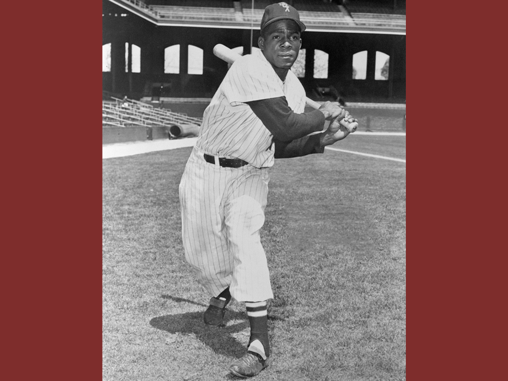Minnie Miñoso poses on a field while poised to swing a bat.