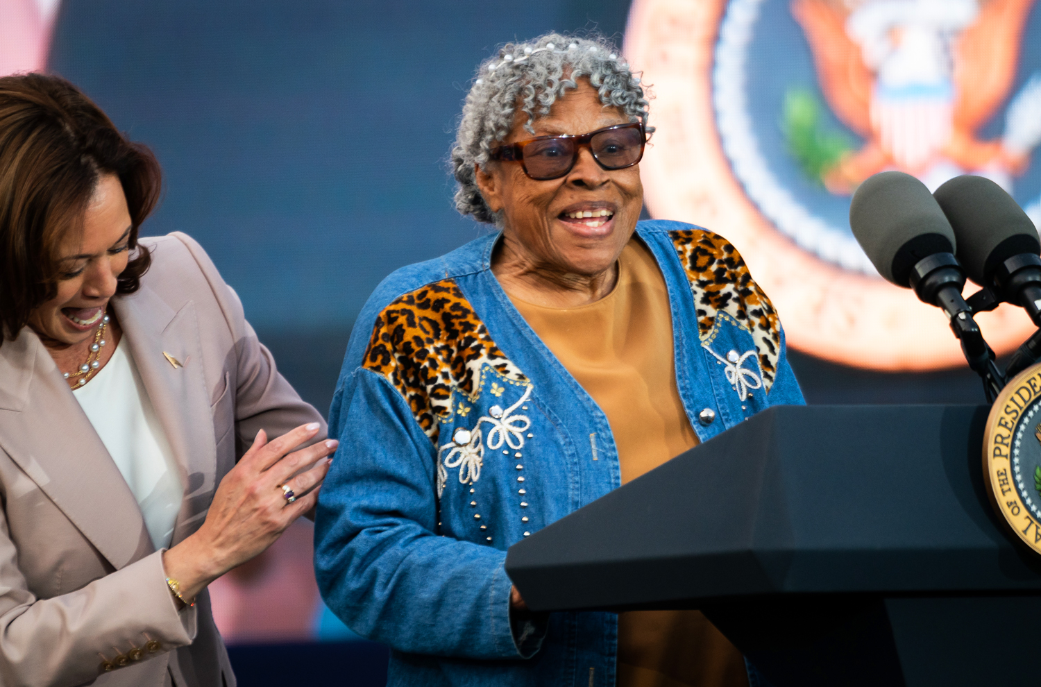 Opal Lee smiles at the presidential podium as Kamala Harris smiles behind her.