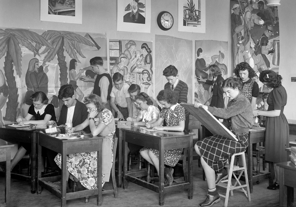 Students draw or paint while surrounded by art in a classroom.
