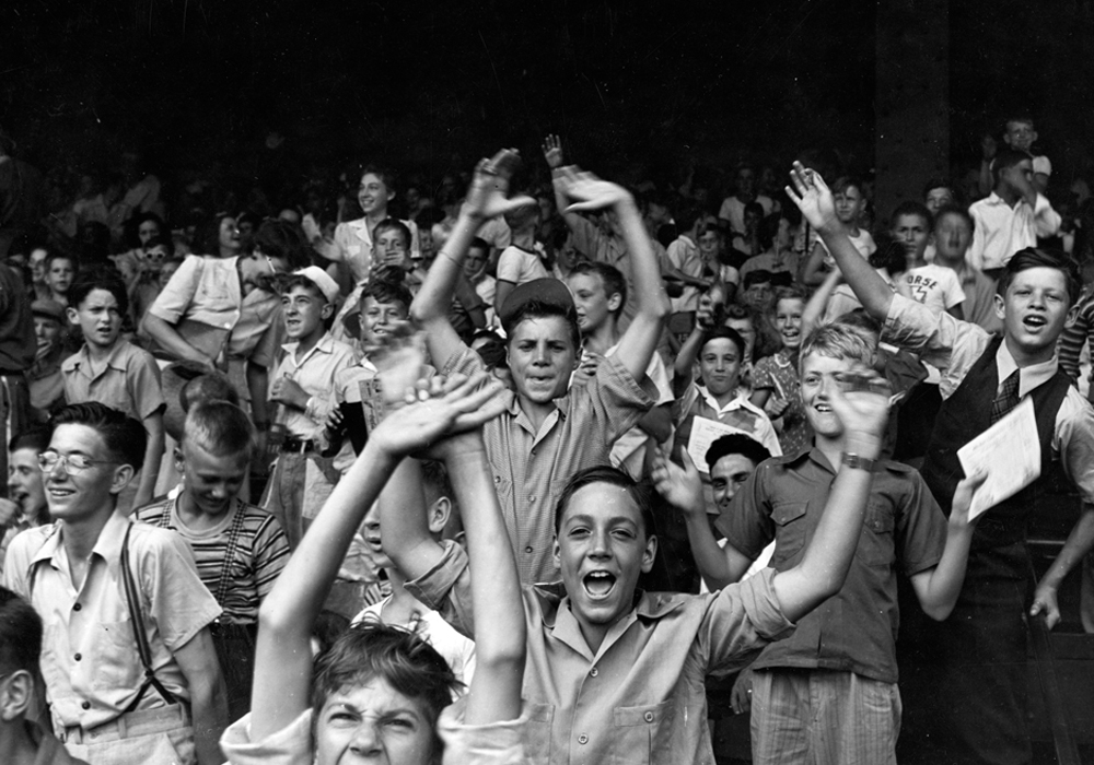 Teenage boys and younger boys cheer in the stands at a sporting event.