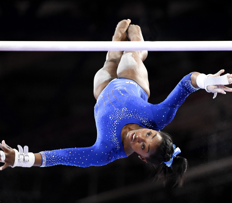 Simone Biles is in midair during an uneven bars routine.