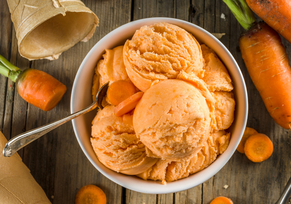 A bowl of orange ice cream is garnished with carrot slices.