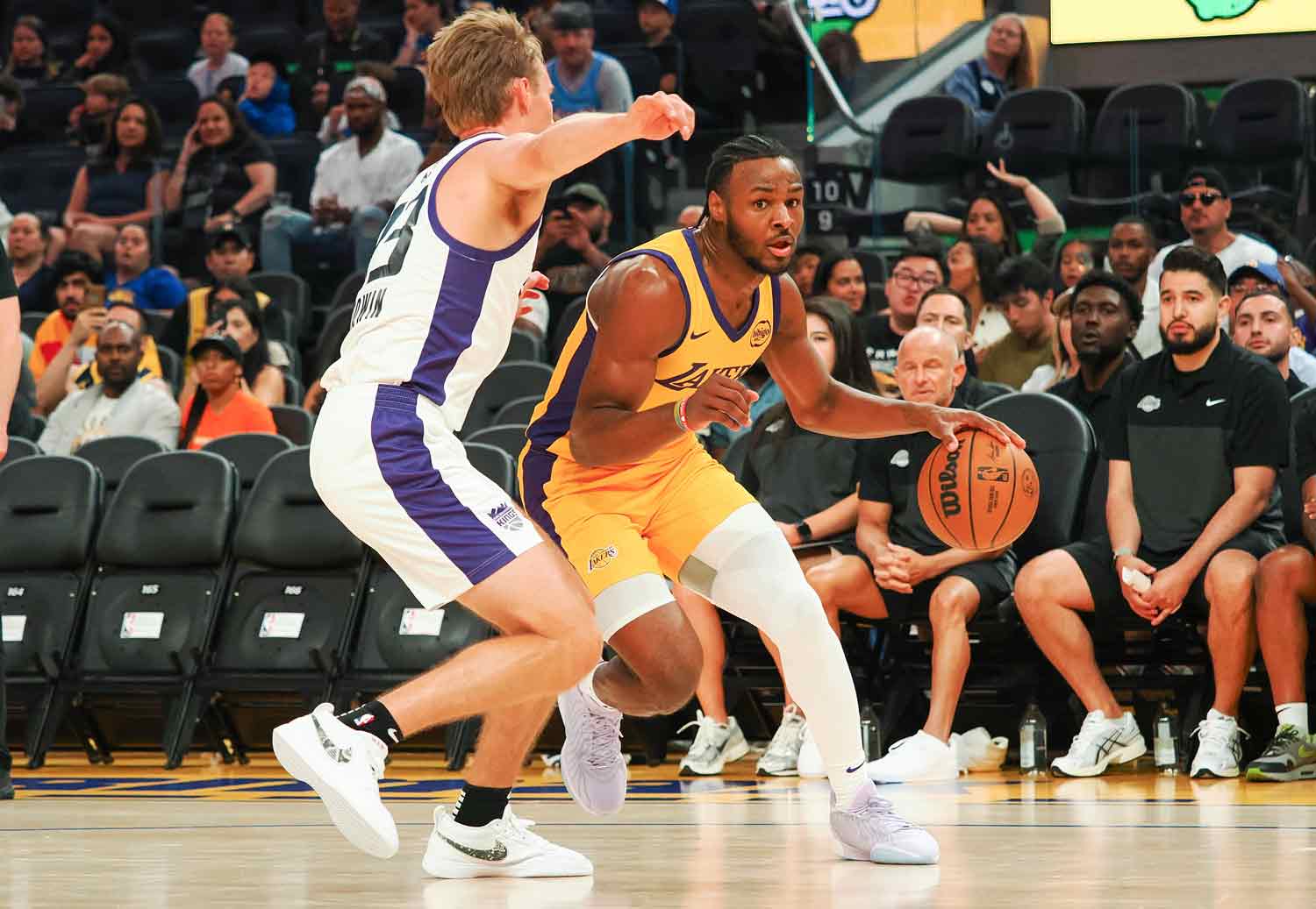 Wearing a Lakers uniform, Bronny James dribbles the ball around an opponent.