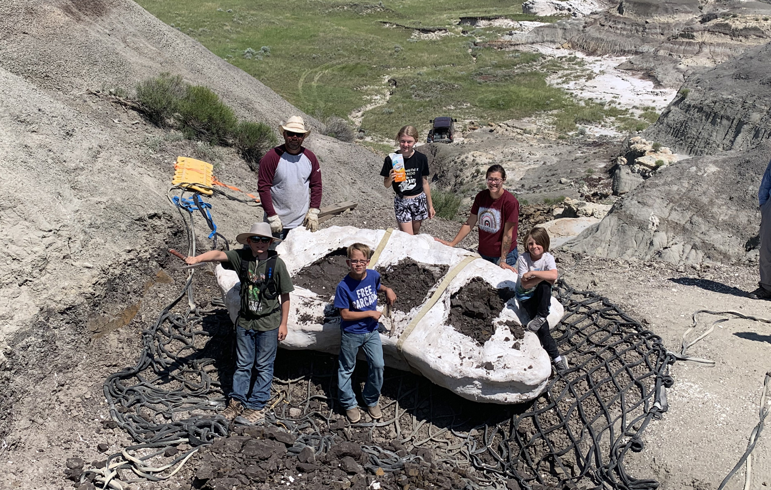 Four children and two adults pose while surrounding a plaster covering of a fossil.