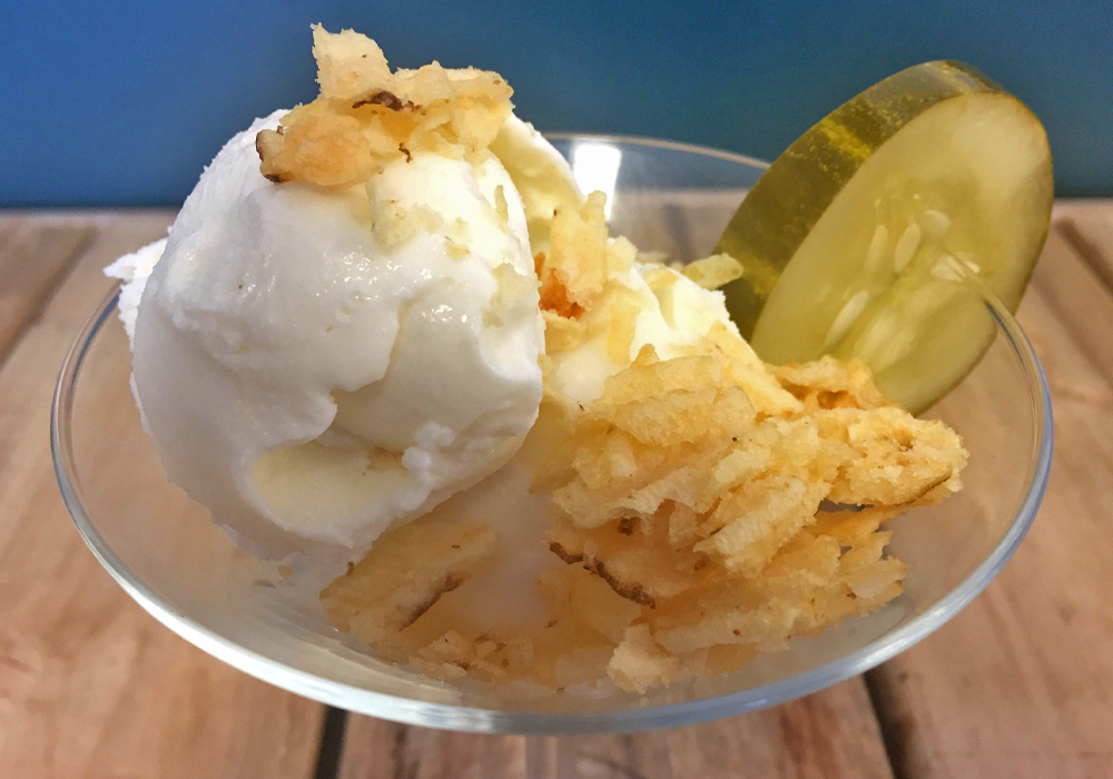 A bowl of white ice cream is garnished with a pickle slice.