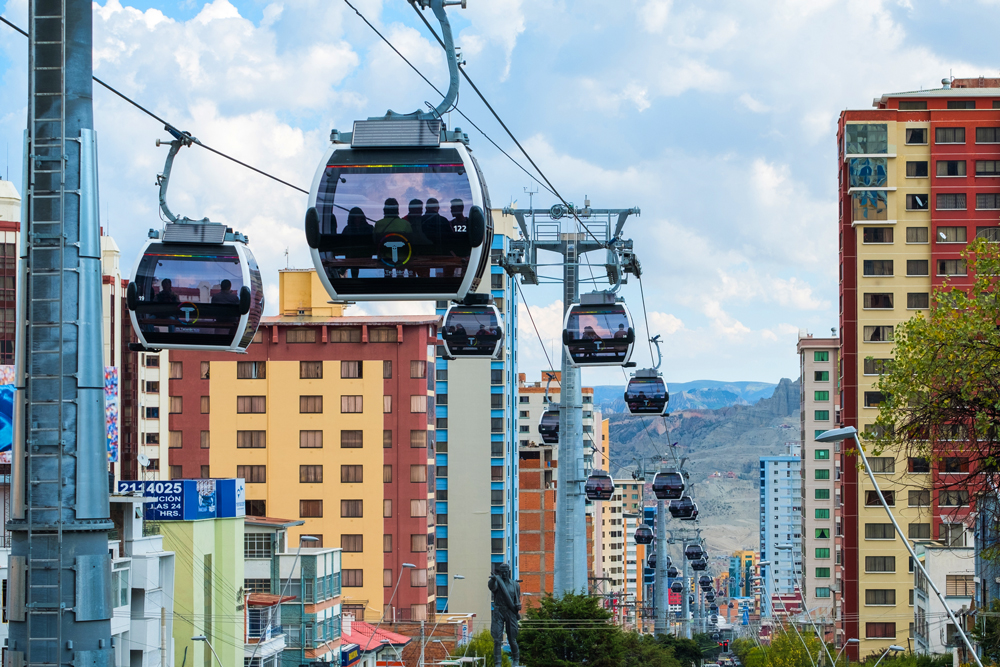 Small gondolas hang from cables above a city and each one holds a few passengers.