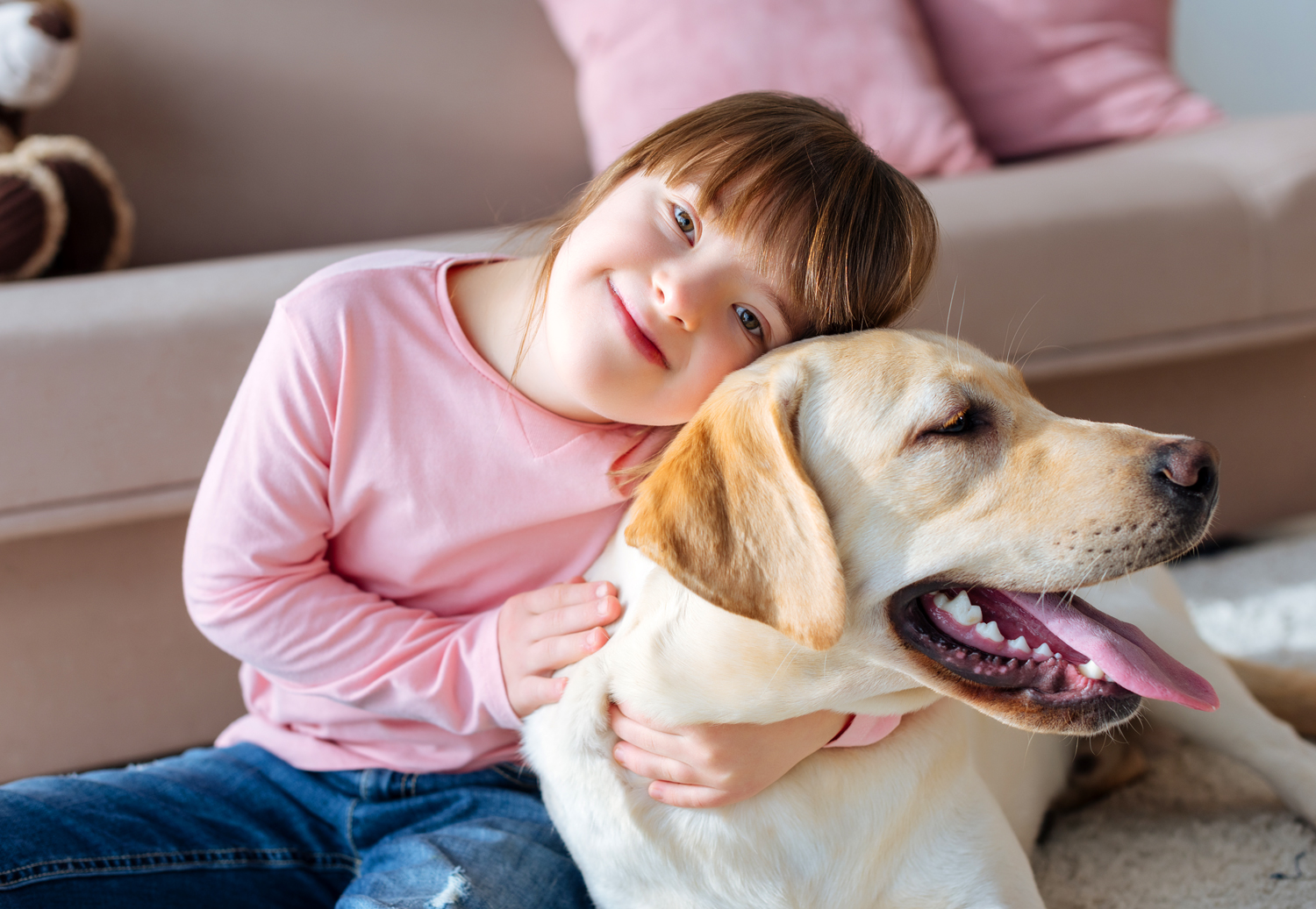 A young girl has her arms around a dog as she looks at the camera.