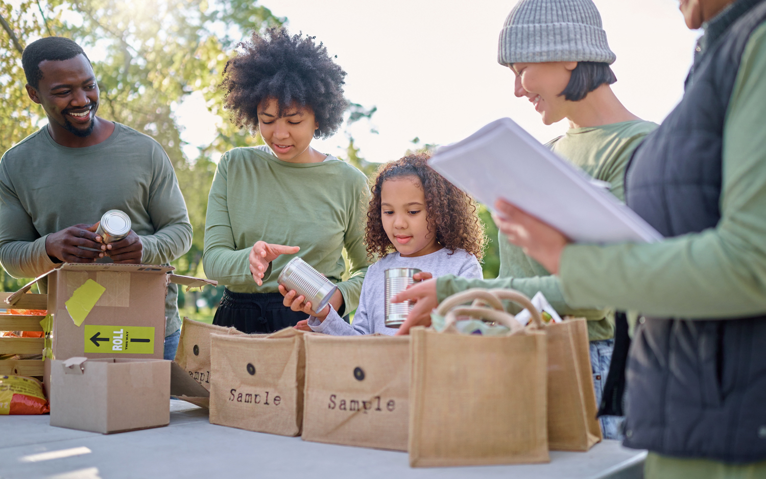 Children and adults stand at a table putting cans in bags.