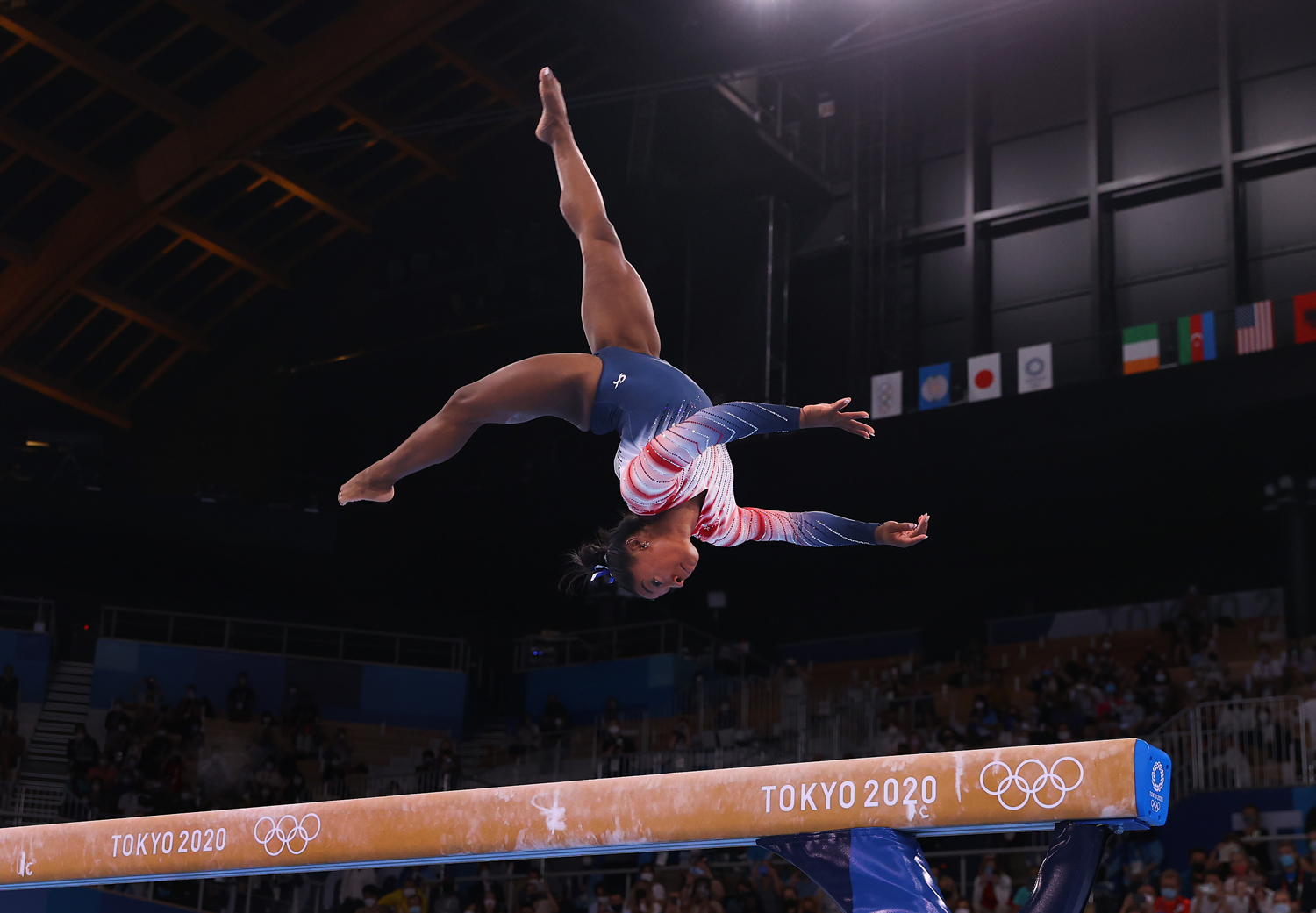 Simone Biles is upside down and in the air as she competes on the balance beam.