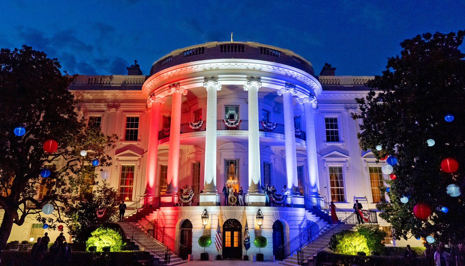 The White House in the evening, lit up with red, white, and blue lights.