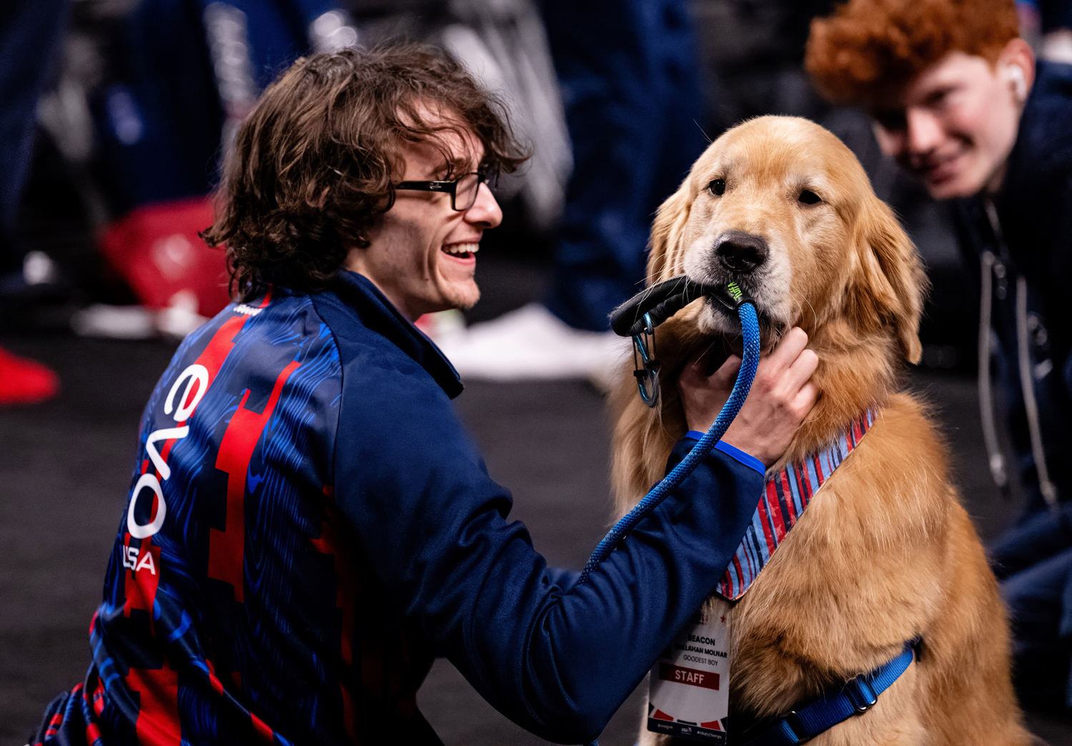 Gymnast Stephen Nedoroscik smiles as he looks at golden retriever Beacon who has a leash in his mouth.