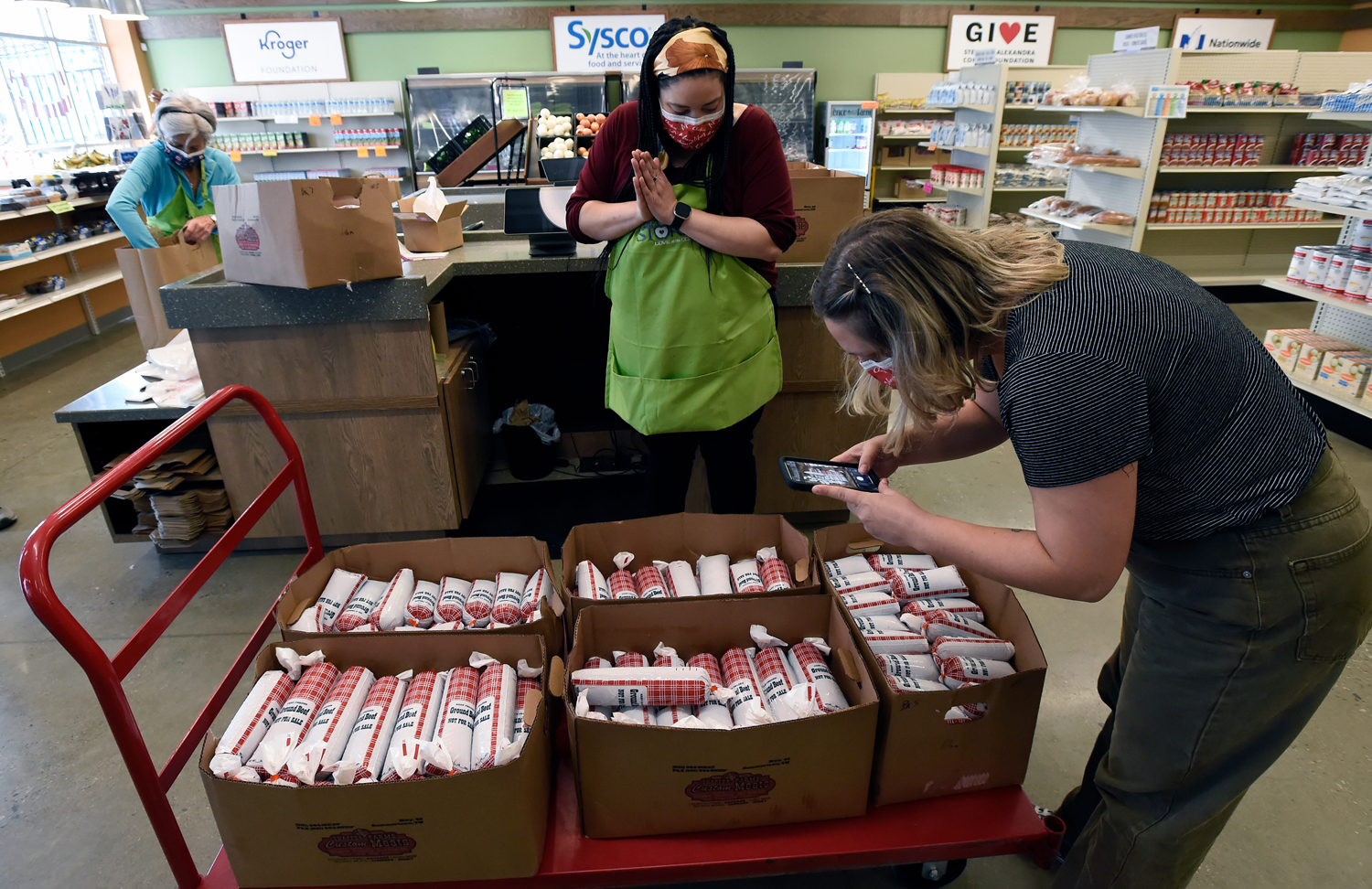 Inside a store, someone takes a photo of boxes of meat as another person watches.