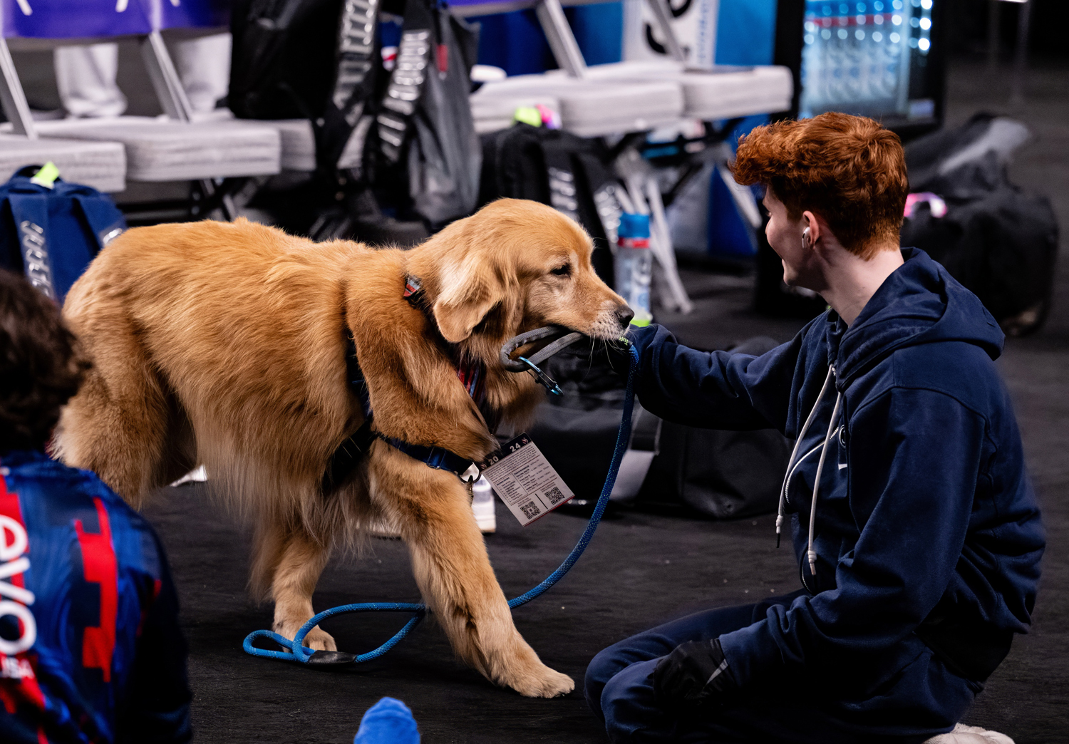 Gymnast Joshua Karnes kneels on the floor and pets Beacon the golden retriever, who is standing.