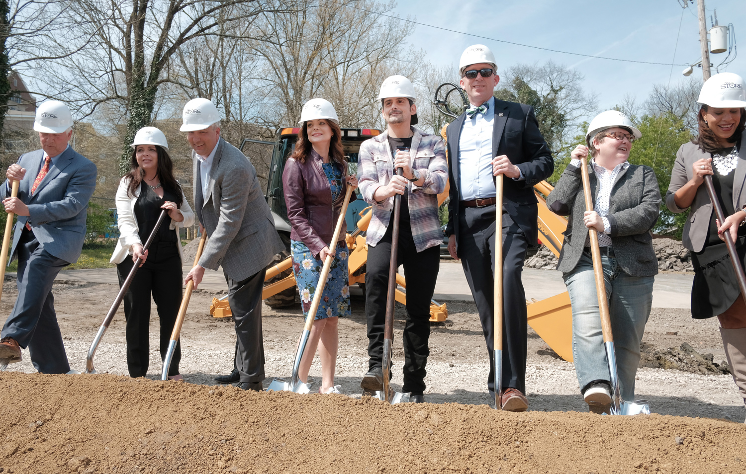 Brad Paisley, Kimberly Williams Paisley, and six other people pose at a groundbreaking wearing hard hats and holding shovels.