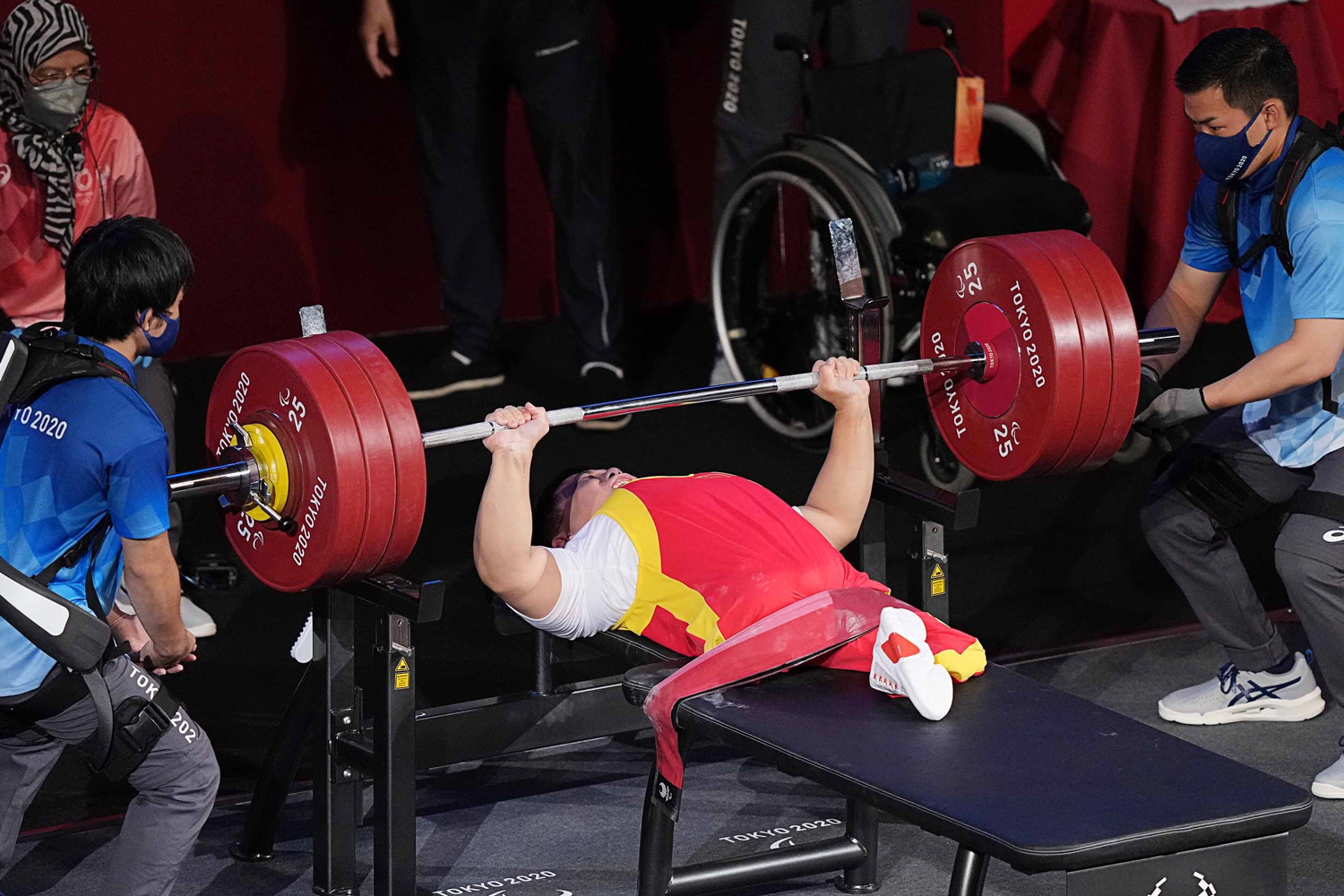 An athlete lies on her back and powerlifts as she is spotted on either side.