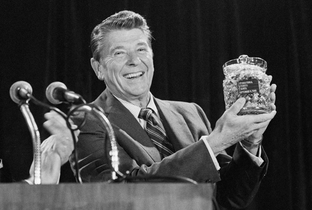 Black and white photo of Ronald Reagan smiling and holding up a glass jar of jellybeans.