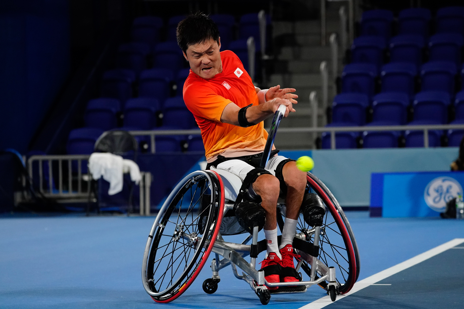 An athlete who uses a wheelchair hits a ball with a racket on a court.