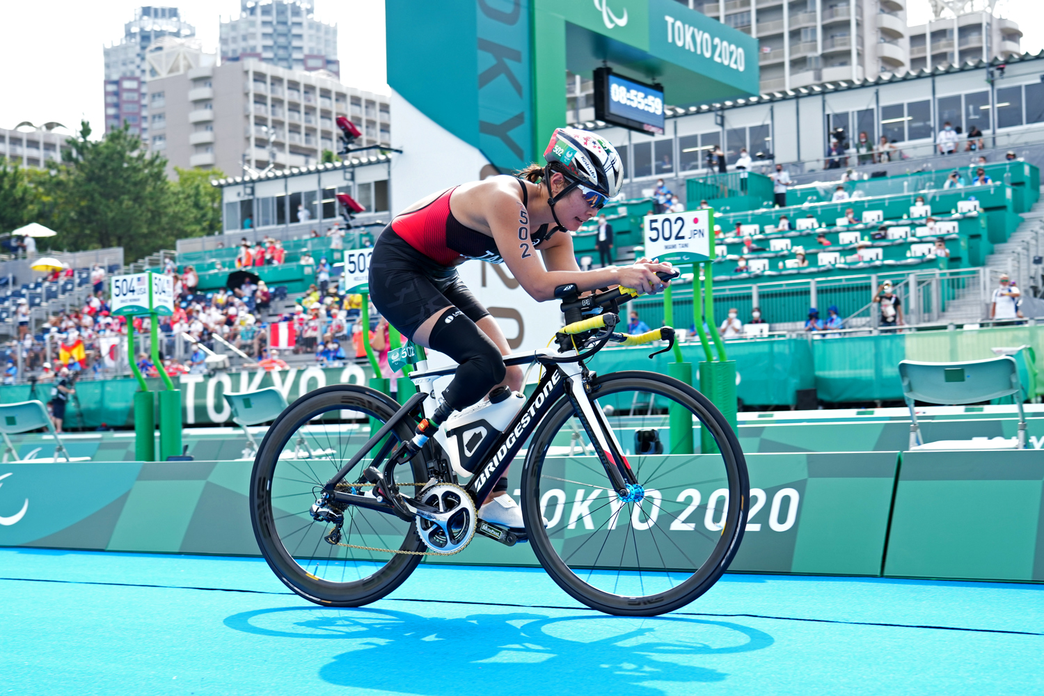 An athlete rides a bike on a track as spectators watch in the stands in the background.