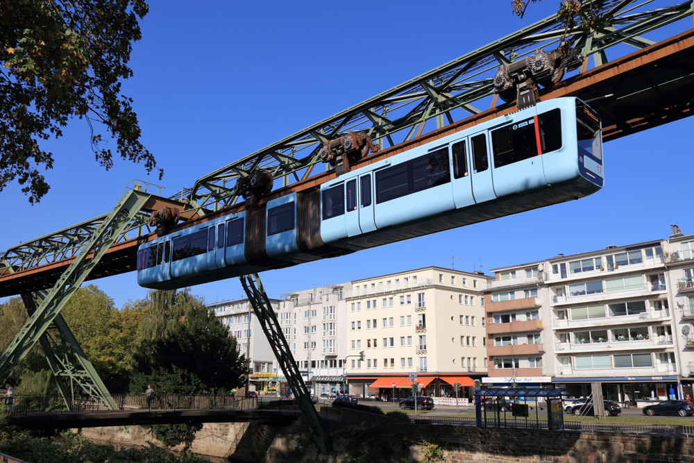 A suspension monorail on a track next to a row of buildings.