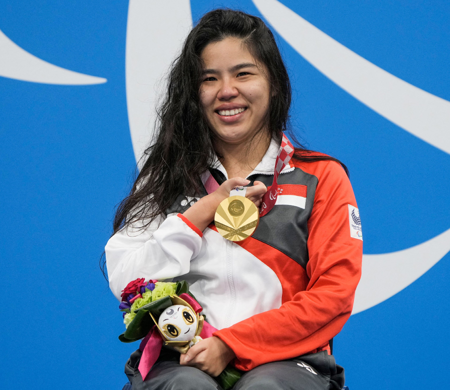 Yip Pin Xiu smiles and holds flowers while showing the Paralympic gold medal that is around her neck.