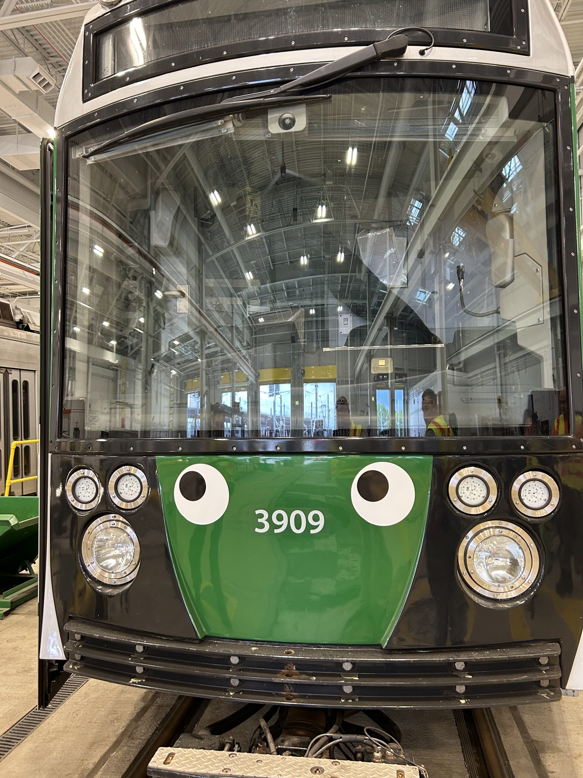 A black subway car with decal eyes on the front leads a number of other cars on an outdoor track.