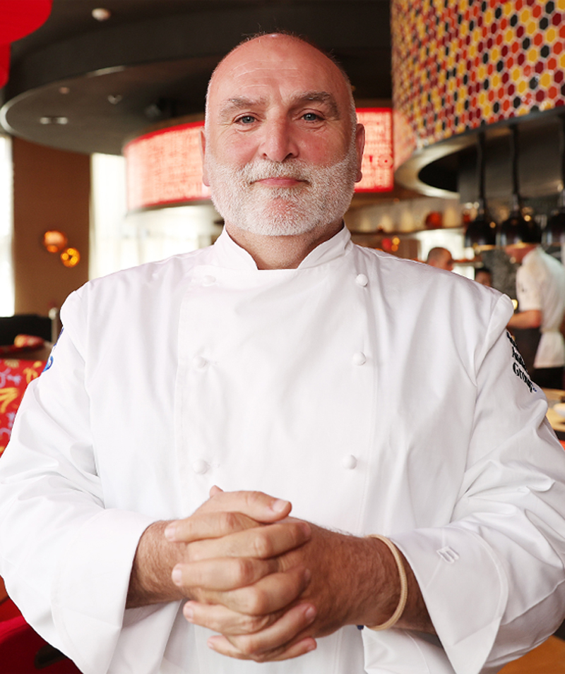 José Andrés poses in a kitchen wearing a chef’s jacket