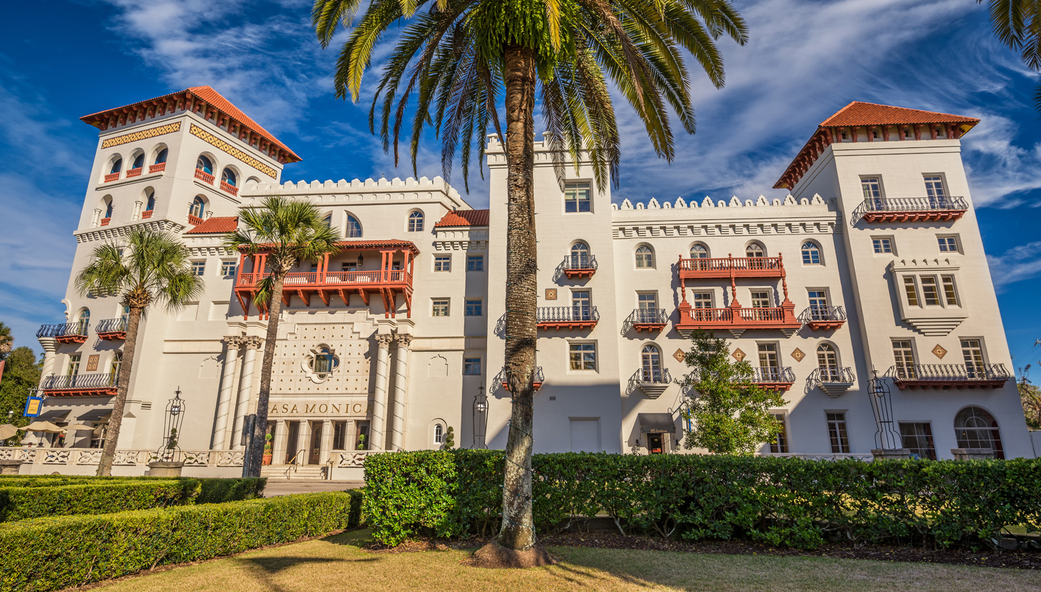 A large, Spanish-style hotel with palm trees in front.