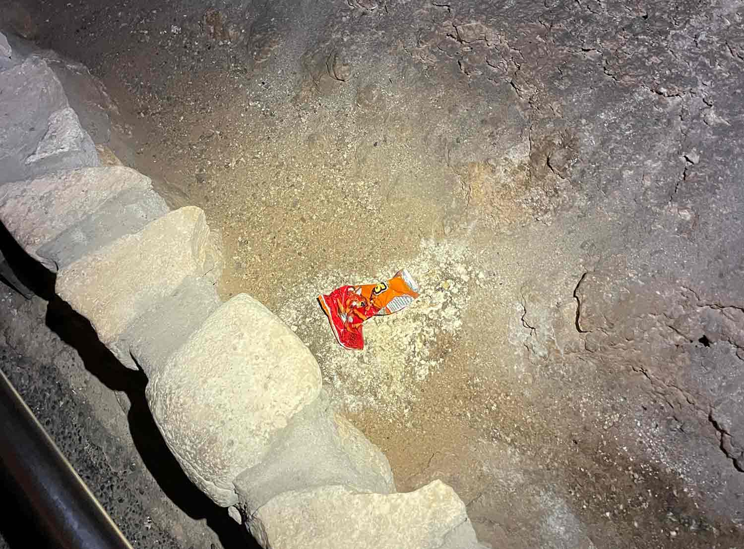 An empty, crumpled Cheetos bag lies on the floor of a cave.