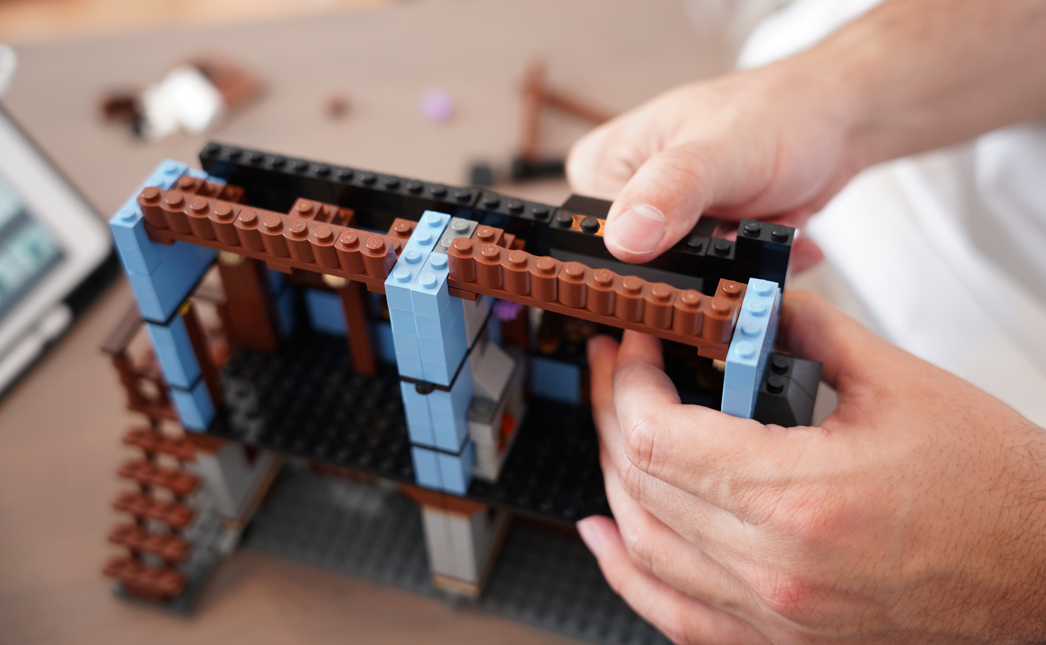 Two hands put together a building with Lego bricks.