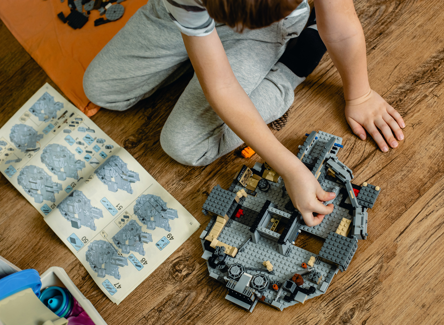 A child sits on the floor and puts together a Millennium Falcon Lego kit.