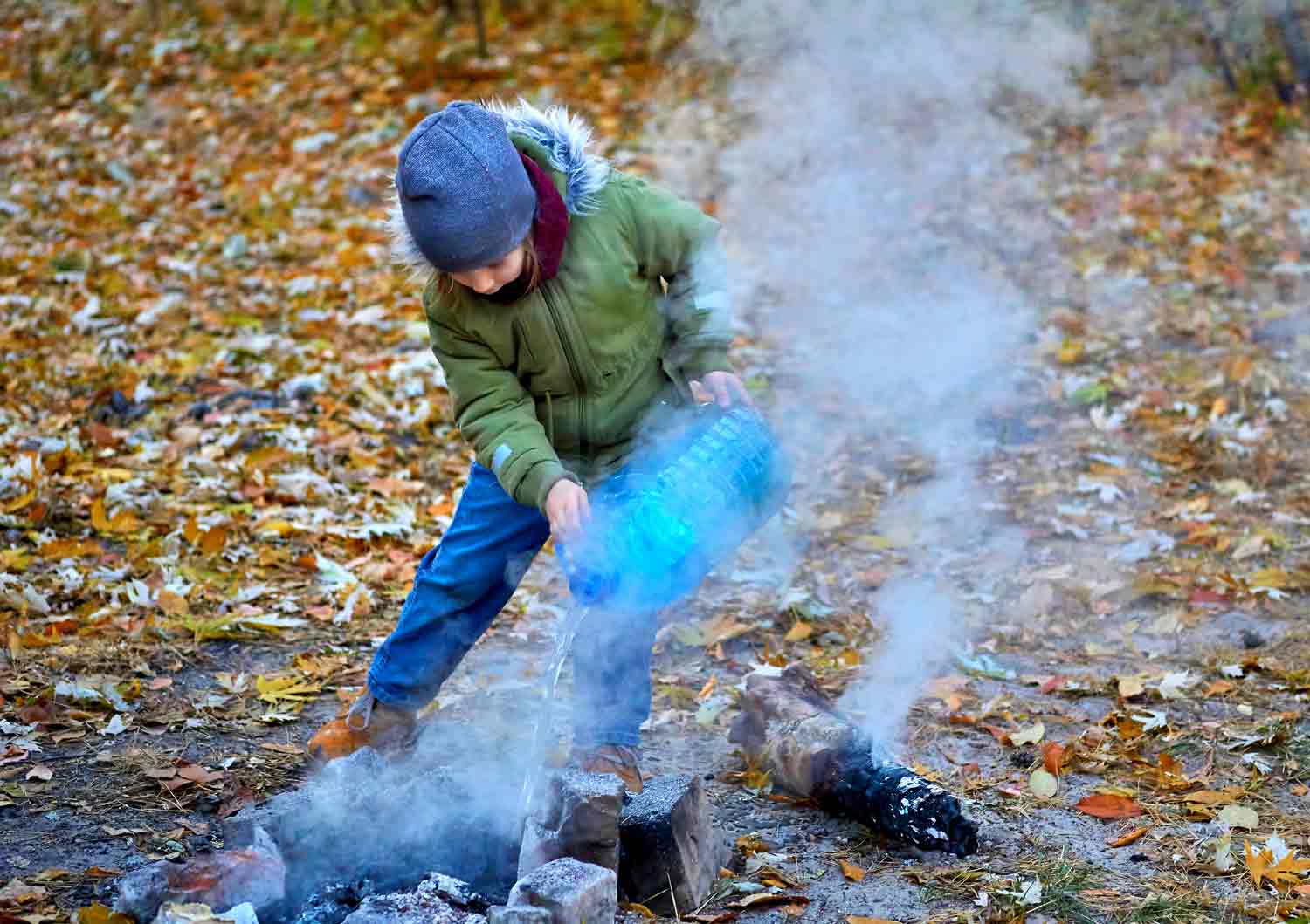 A child uses a large bottle of water to put out a campfire.