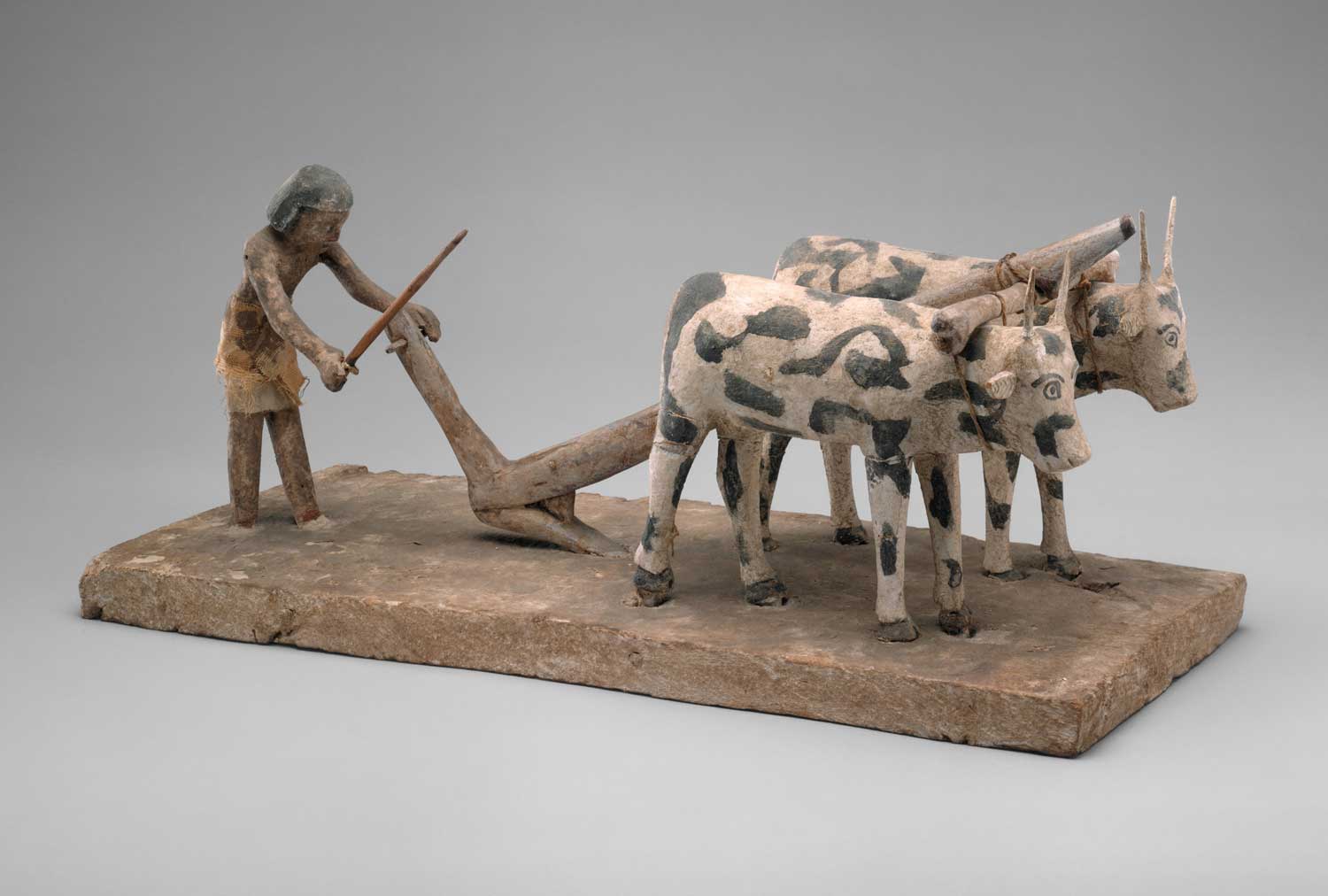 A sculpture of an ancient Egyptian man using a plow led by two oxen.