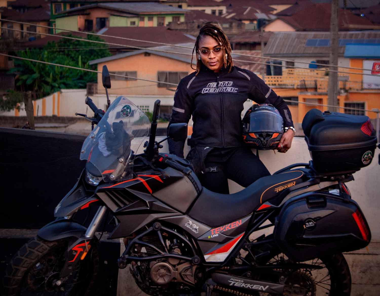 Udoh Ebaide Joy poses behind her motorcycle holding her helmet.