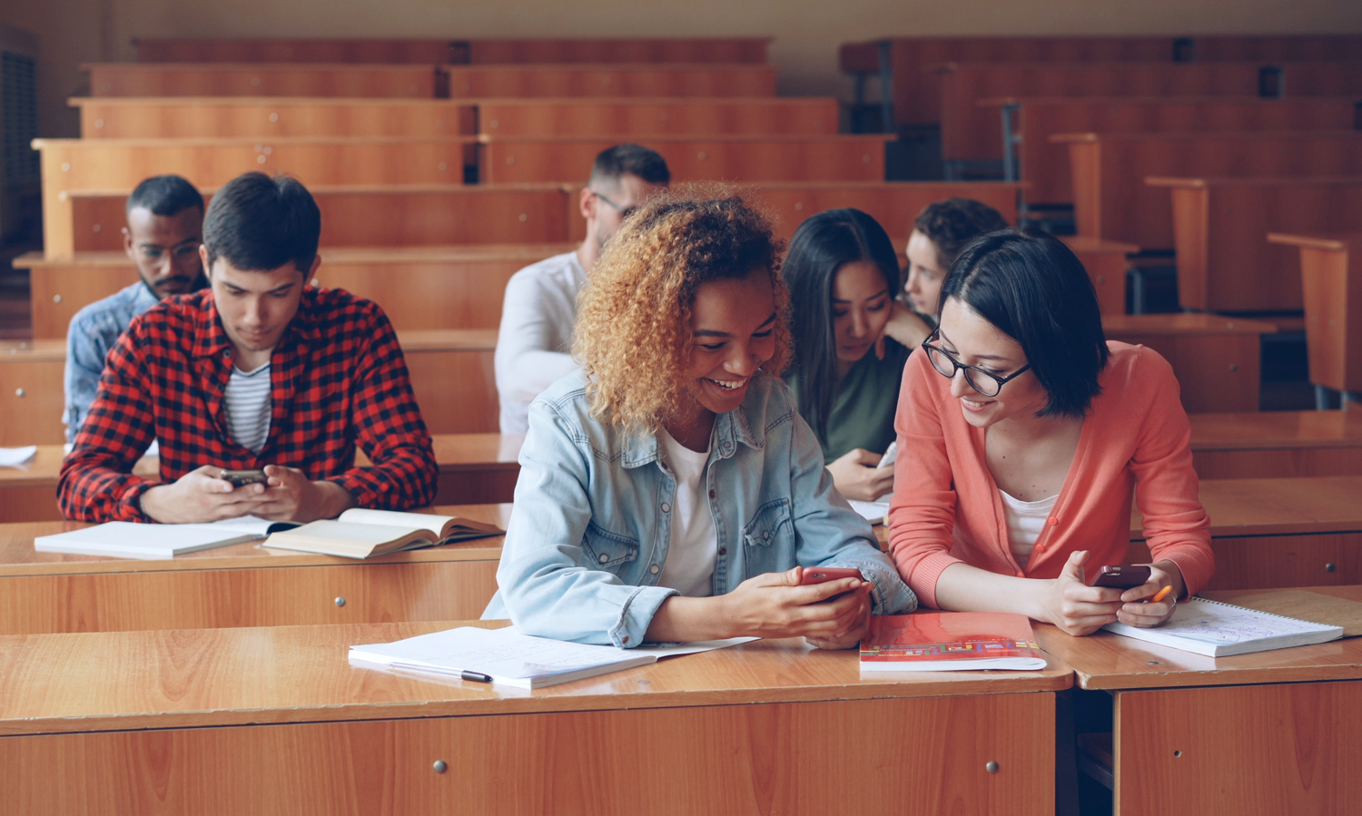 College students look at their phones while sitting in a lecture hall.