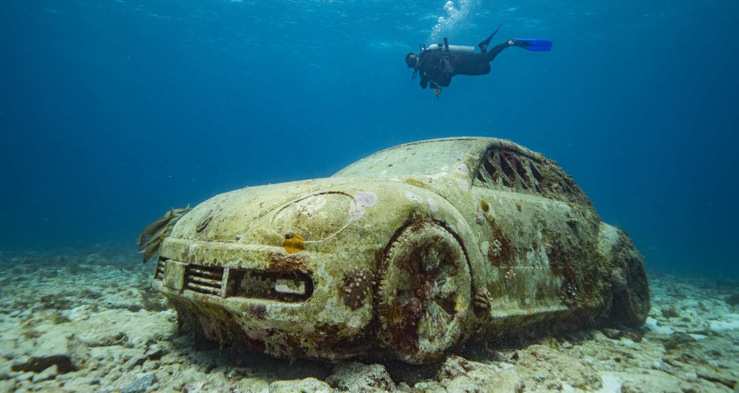 A diver swims past an underwater sculpture of a Volkswagen Beetle.