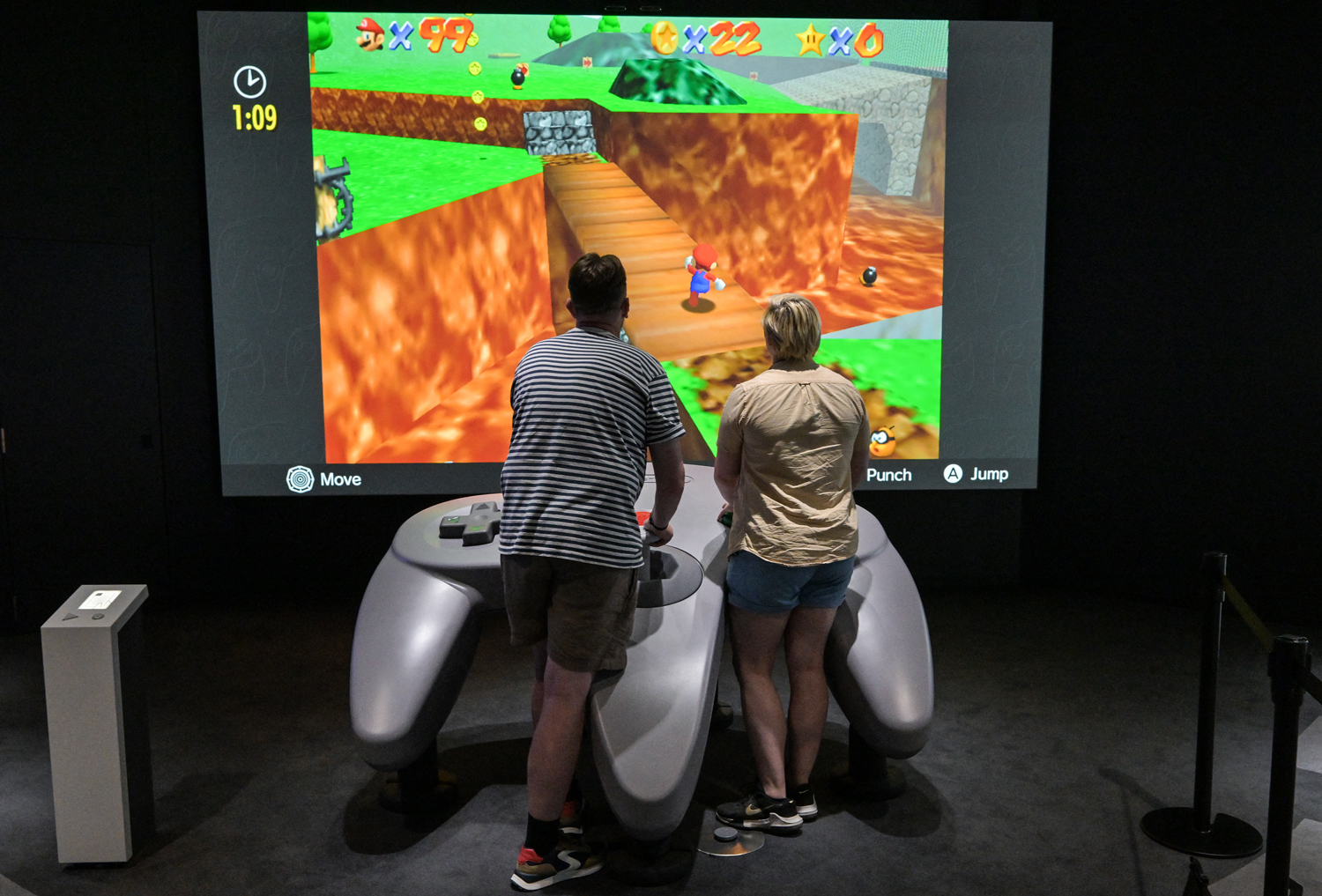 Two people play a video game using a giant controller.