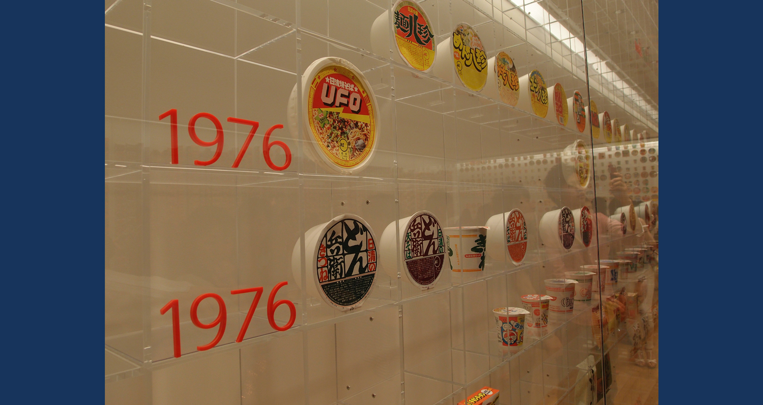 Different versions of Cup Noodles packaging are in a display case on which different years are labeled.