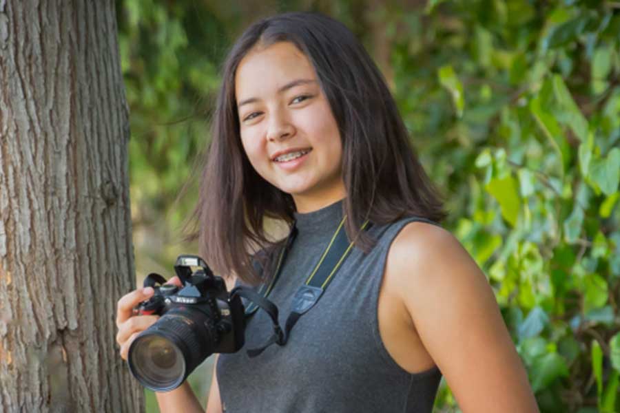 A teen poses while holding a camera.