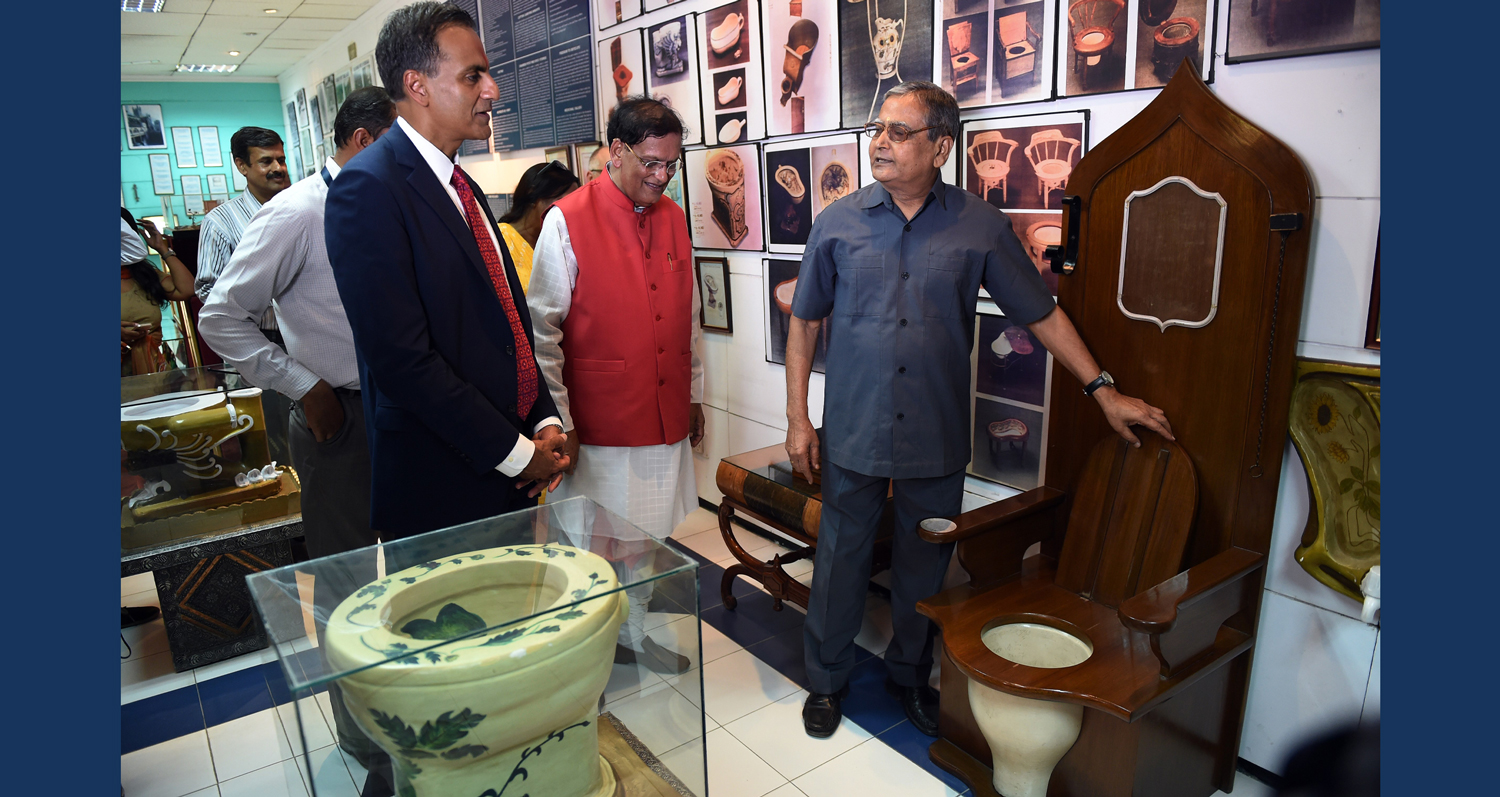 A man shows a wooden toilet throne to a group of visitors in a room full of unusual toilets.